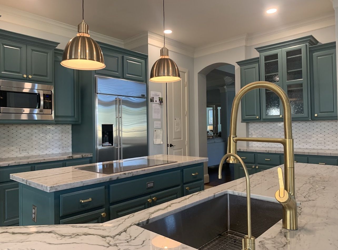Teal kitchen with marble island, stainless fridge, brass pendant lights, and farmhouse sink.