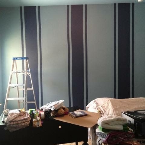 Bedroom with striped gray walls, a ladder, and stacked clothes and bags on furniture.