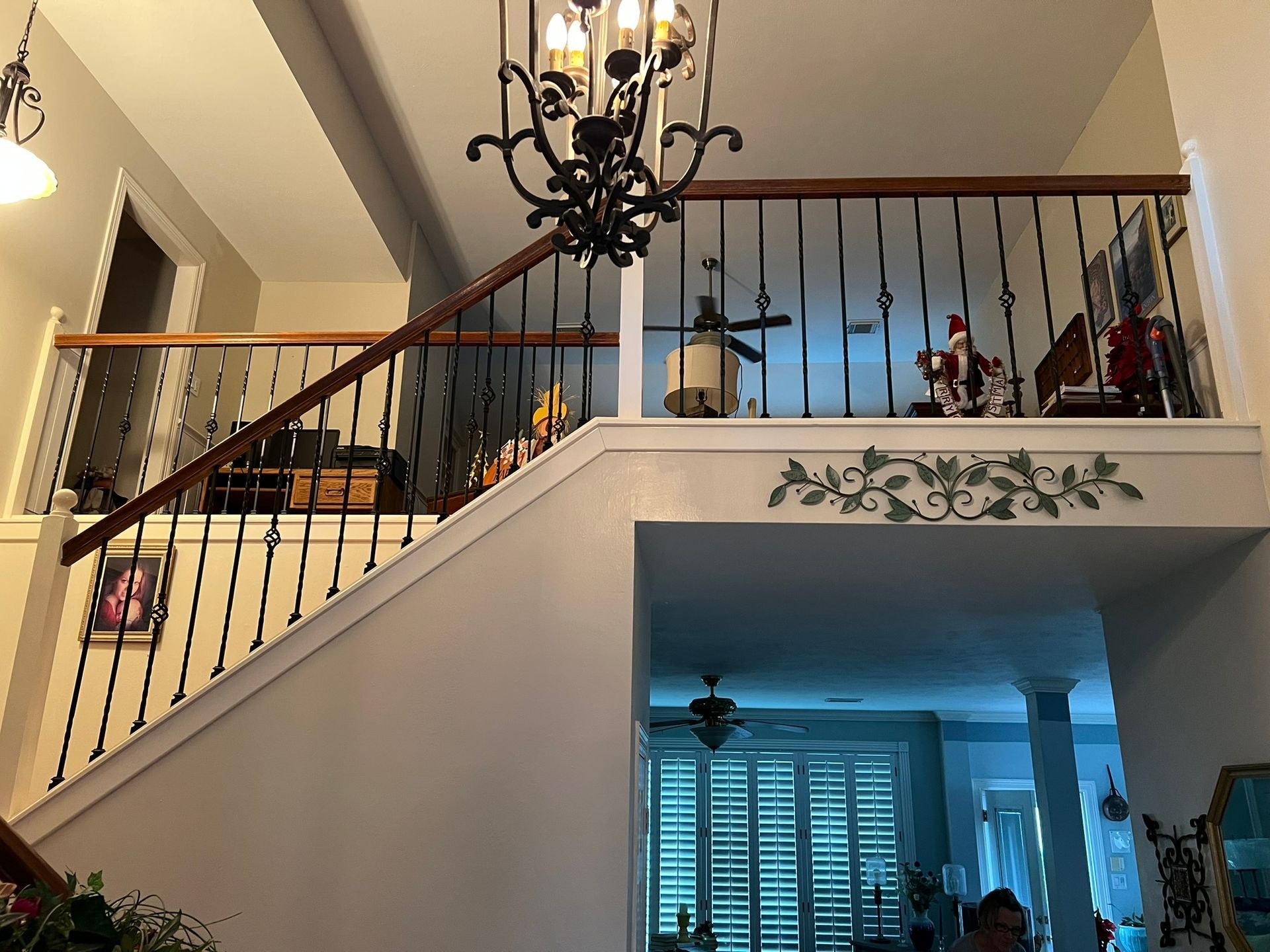 Staircase foyer with black chandelier, wood banister, and a view into a blue-lit living room