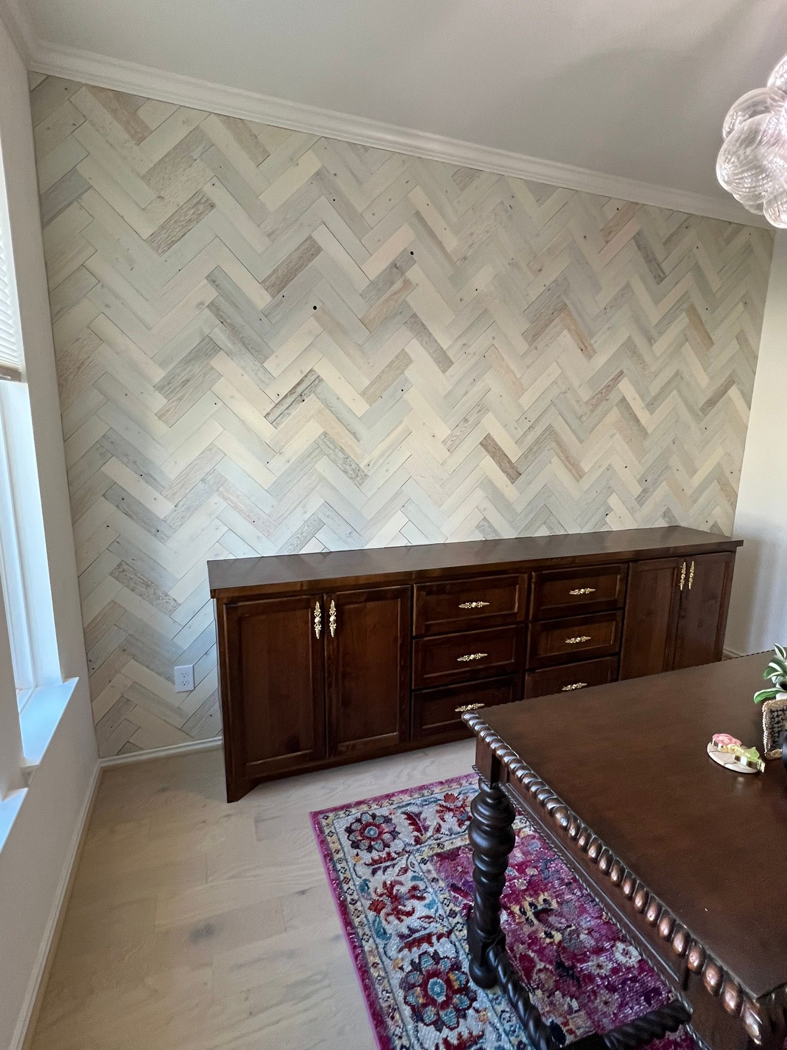 Dining room with chevron-patterned wall, dark wood sideboard, and ornate table in the foreground