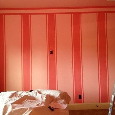 A room with pink striped walls, a bed with white bedding, and a small table in front.