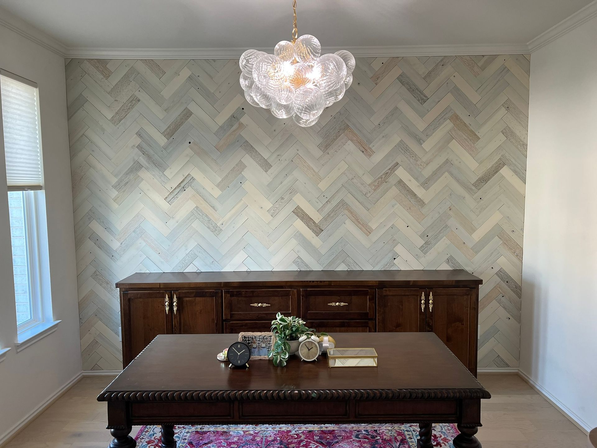 Dining room with chevron wallpaper, dark wood table and sideboard, and a clear glass chandelier.