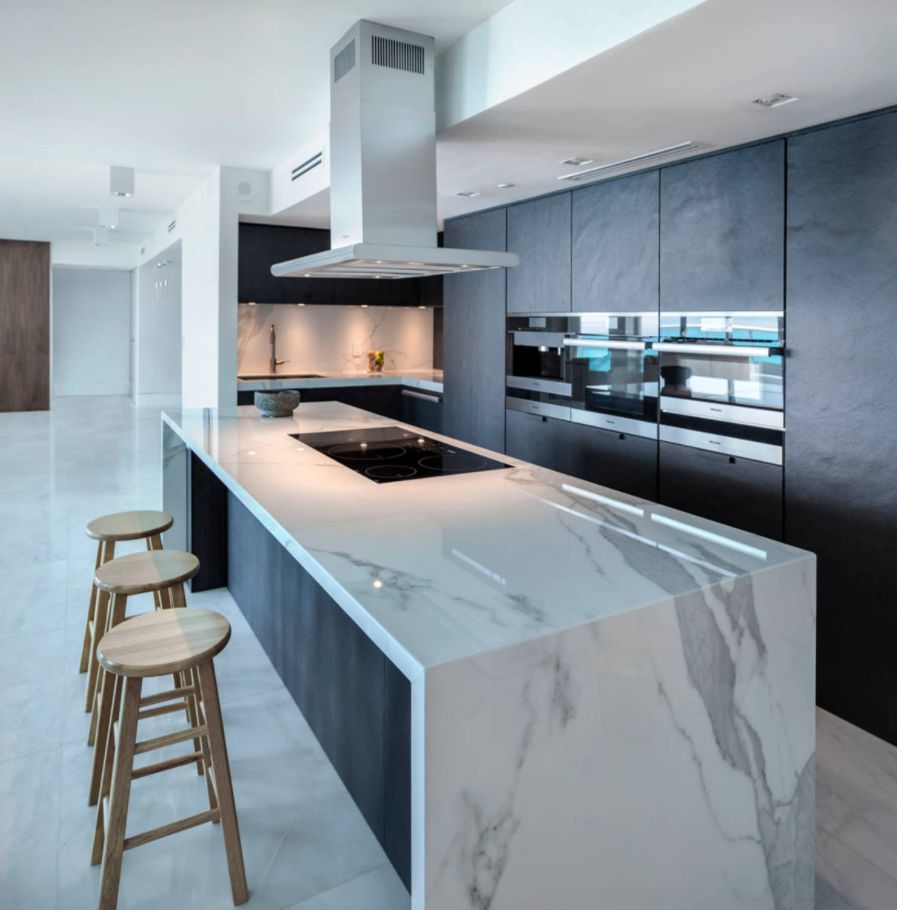 Modern kitchen with a marble island, three stools, dark cabinetry, and stainless steel appliances