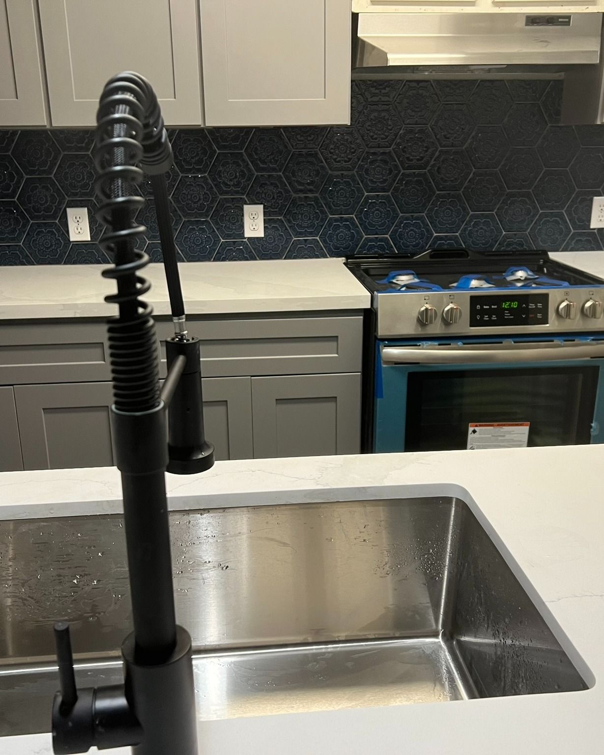 Kitchen sink with tall black faucet in a modern gray kitchen, with stove and cabinets in the background