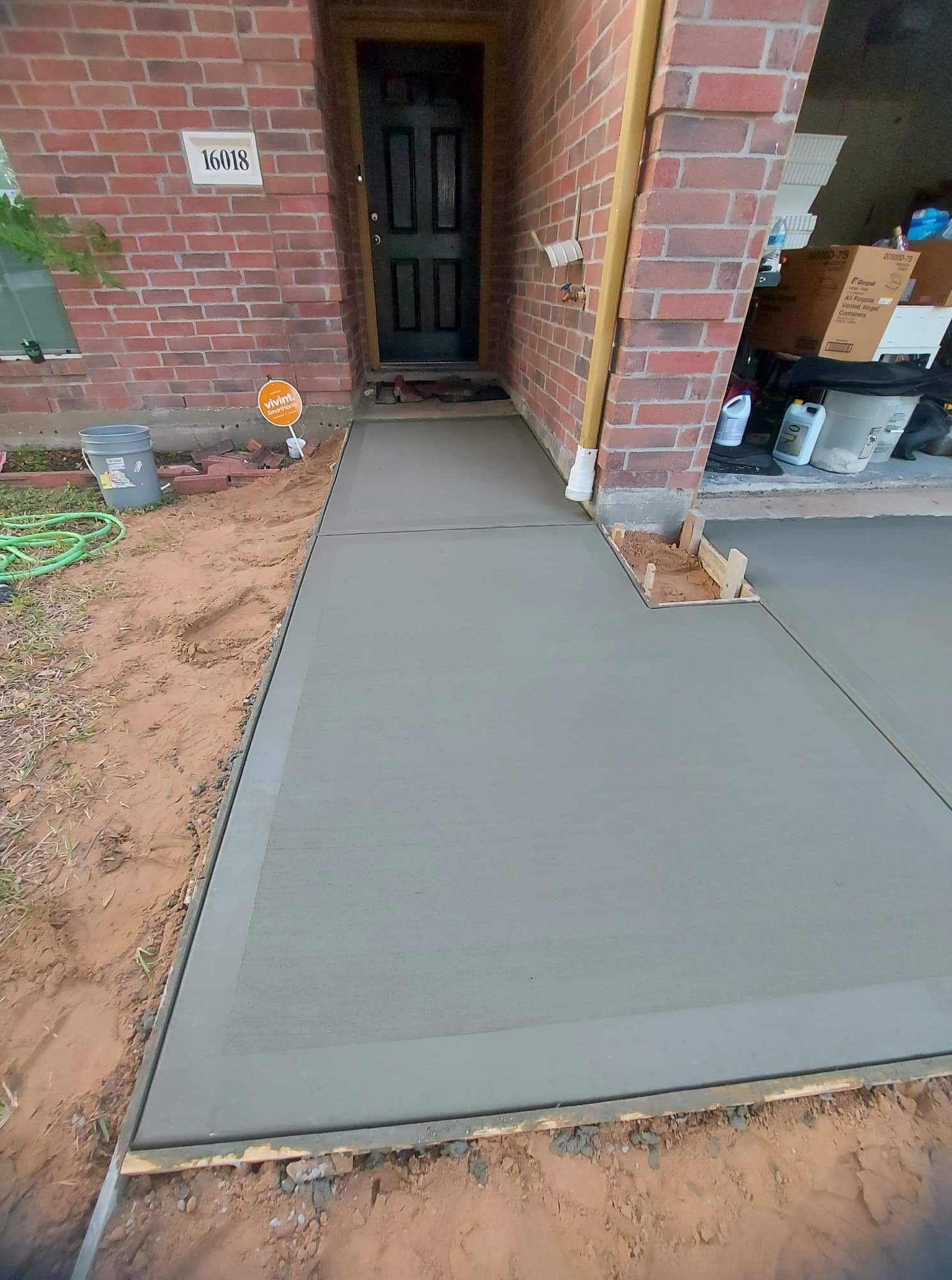 New gray concrete walkway leading to a front doorway beside a brick house under construction