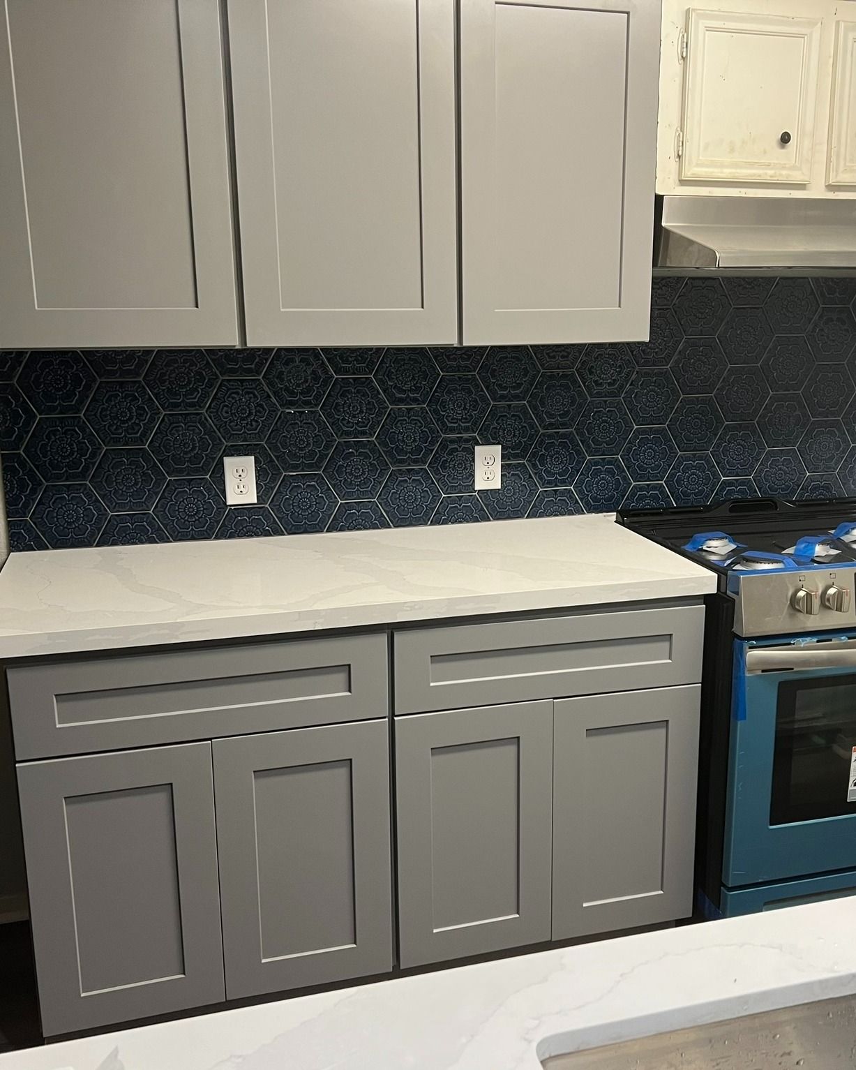 Gray kitchen cabinets, white countertop, dark backsplash, and a blue stove in a modern kitchen.