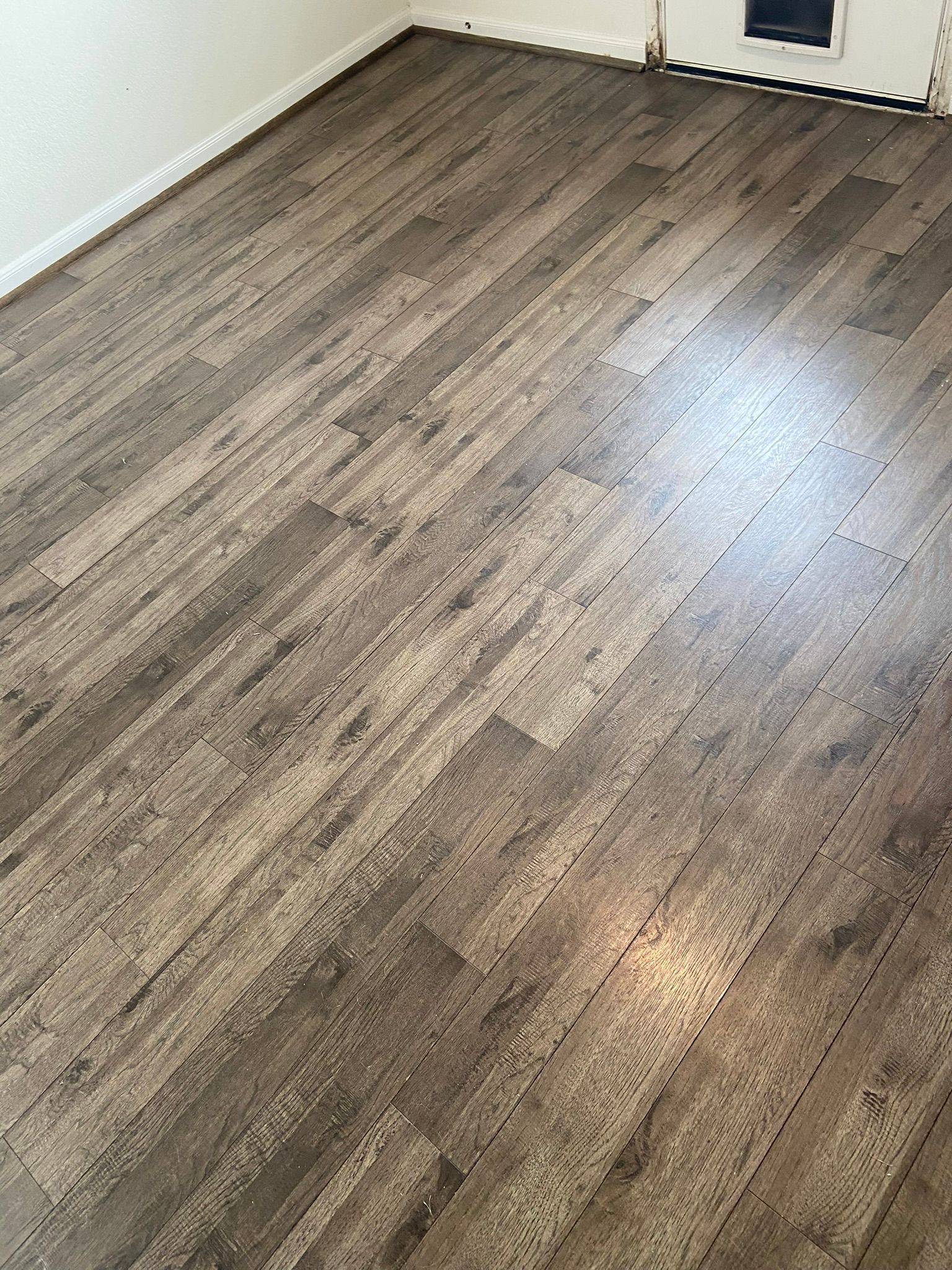 Empty room with wood-look flooring and white walls, lit by sunlight from a window.
