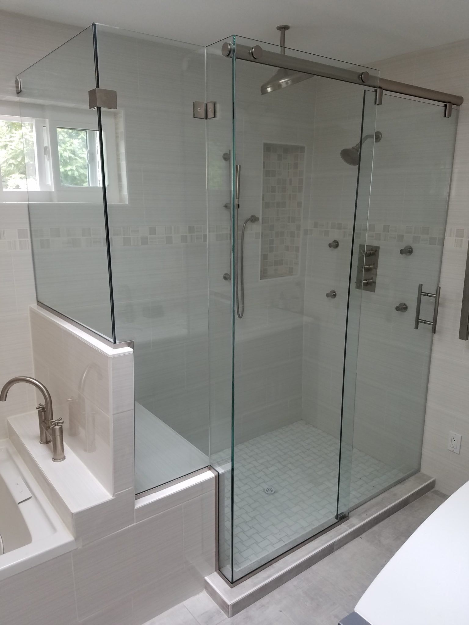 Modern bathroom with a glass-enclosed shower, white tile, and a nearby sink countertop.