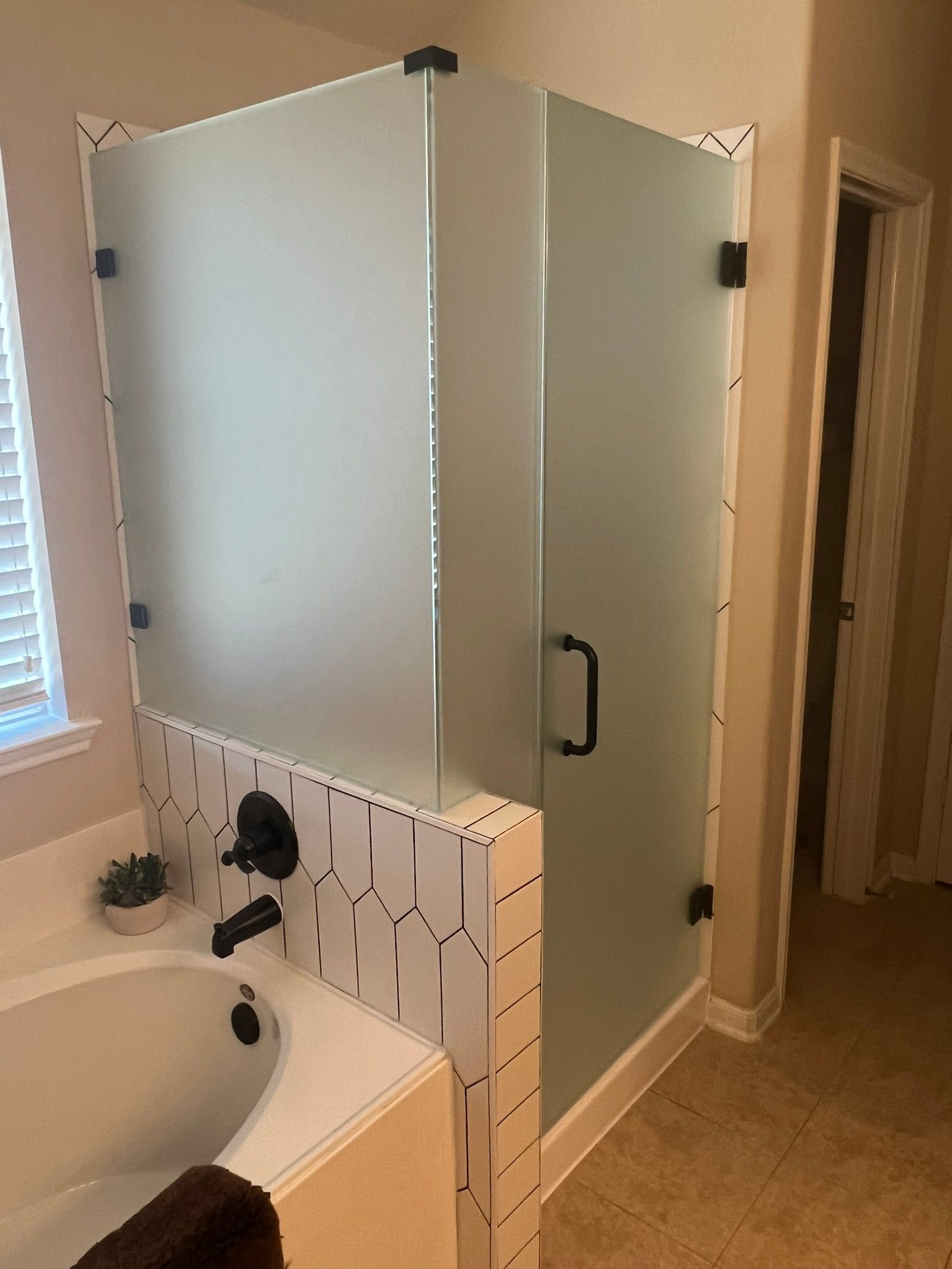Bathroom with frosted-glass shower enclosure beside a sink and toilet area, in neutral beige tones