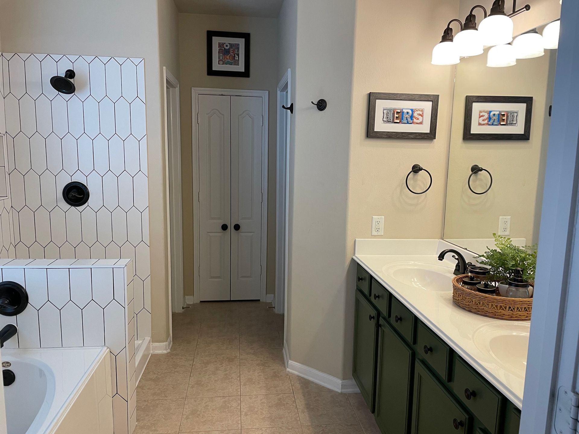 Bathroom with white vanity, green cabinets, bathtub with white tile, and open door to a hallway