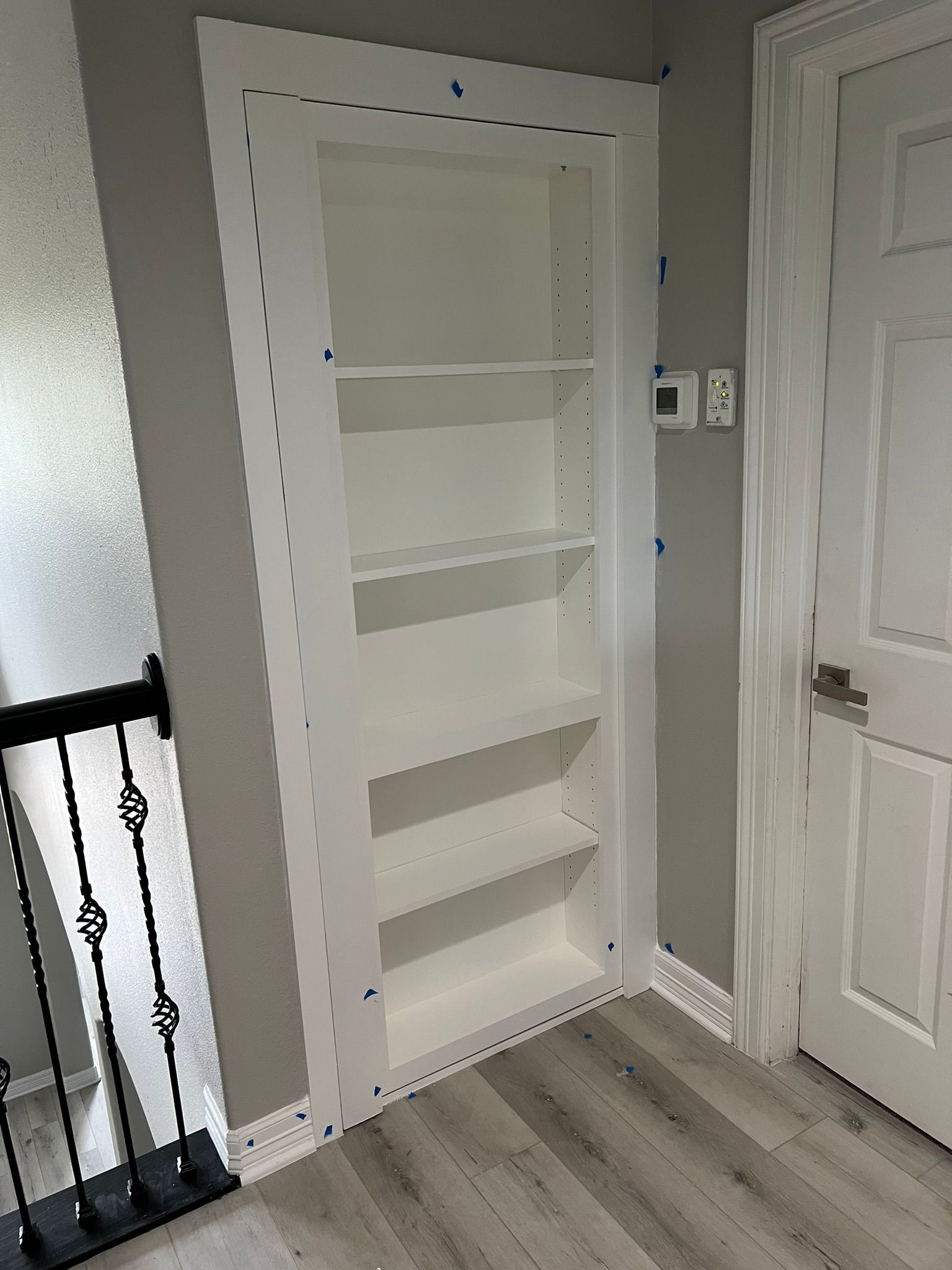 Built-in white shelving unit beside a doorway in a light gray hallway