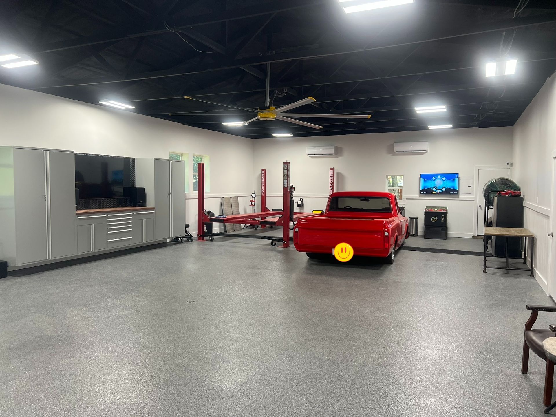 Spacious auto shop with a red car, tool cabinets, lift equipment, and a polished gray floor.