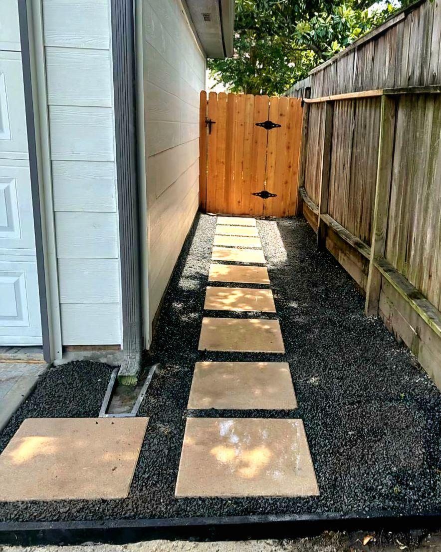 Narrow side yard walkway with stepping stones, gravel, and a wooden gate between house and fence.