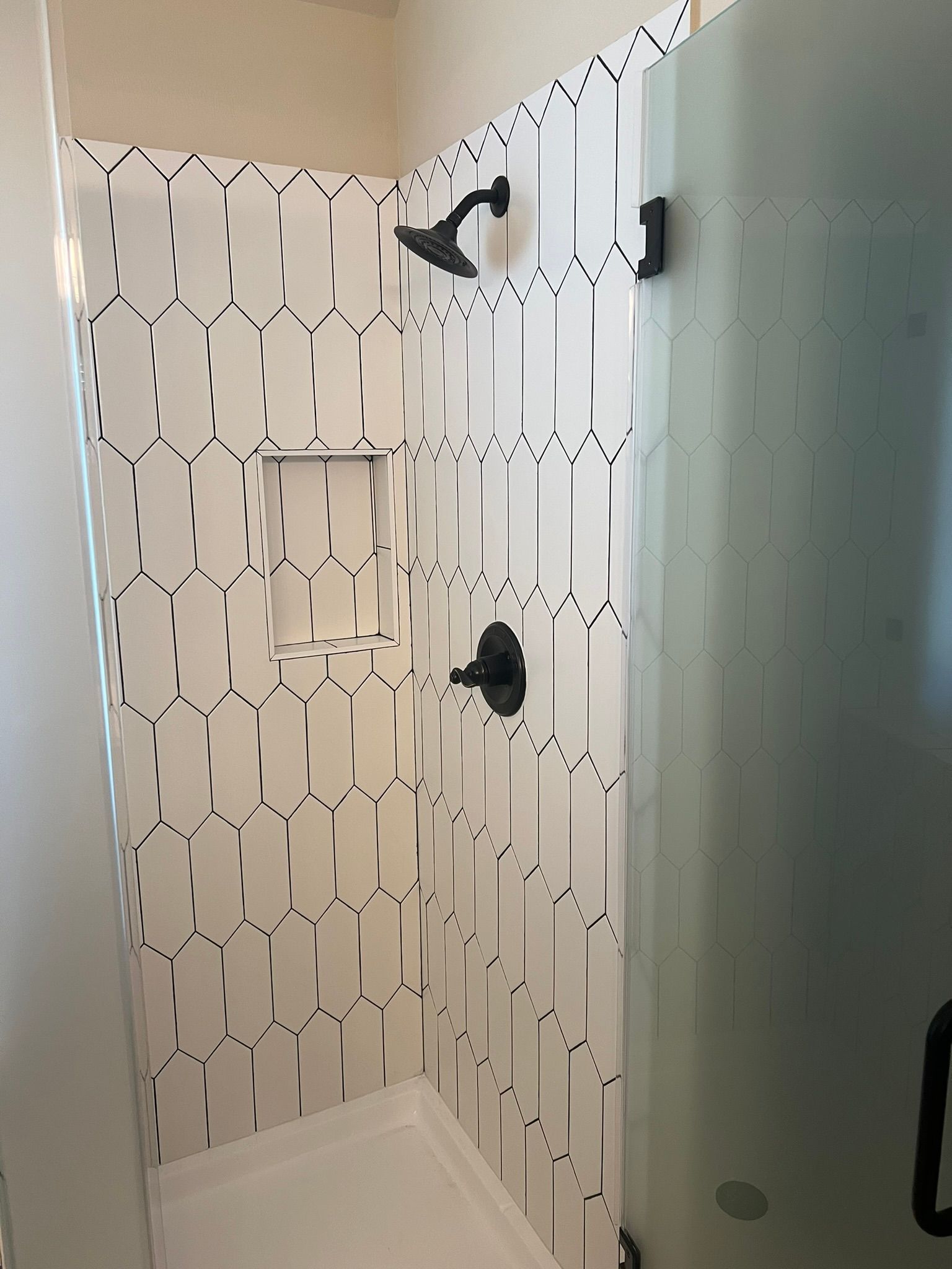 Small bathroom shower with white patterned tile, black shower fixtures, and a frosted glass door.
