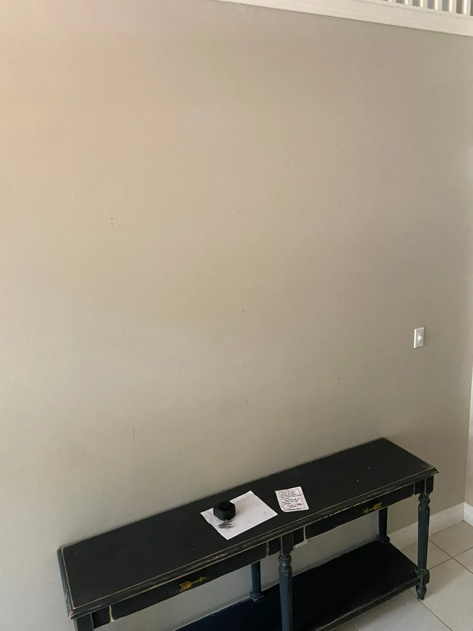 Black console table against a beige wall with a few papers on top.