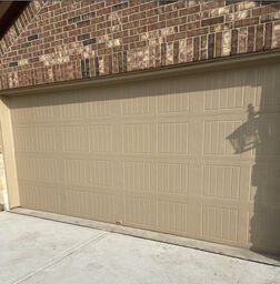 Beige garage door beneath brick facade, with concrete driveway in front.