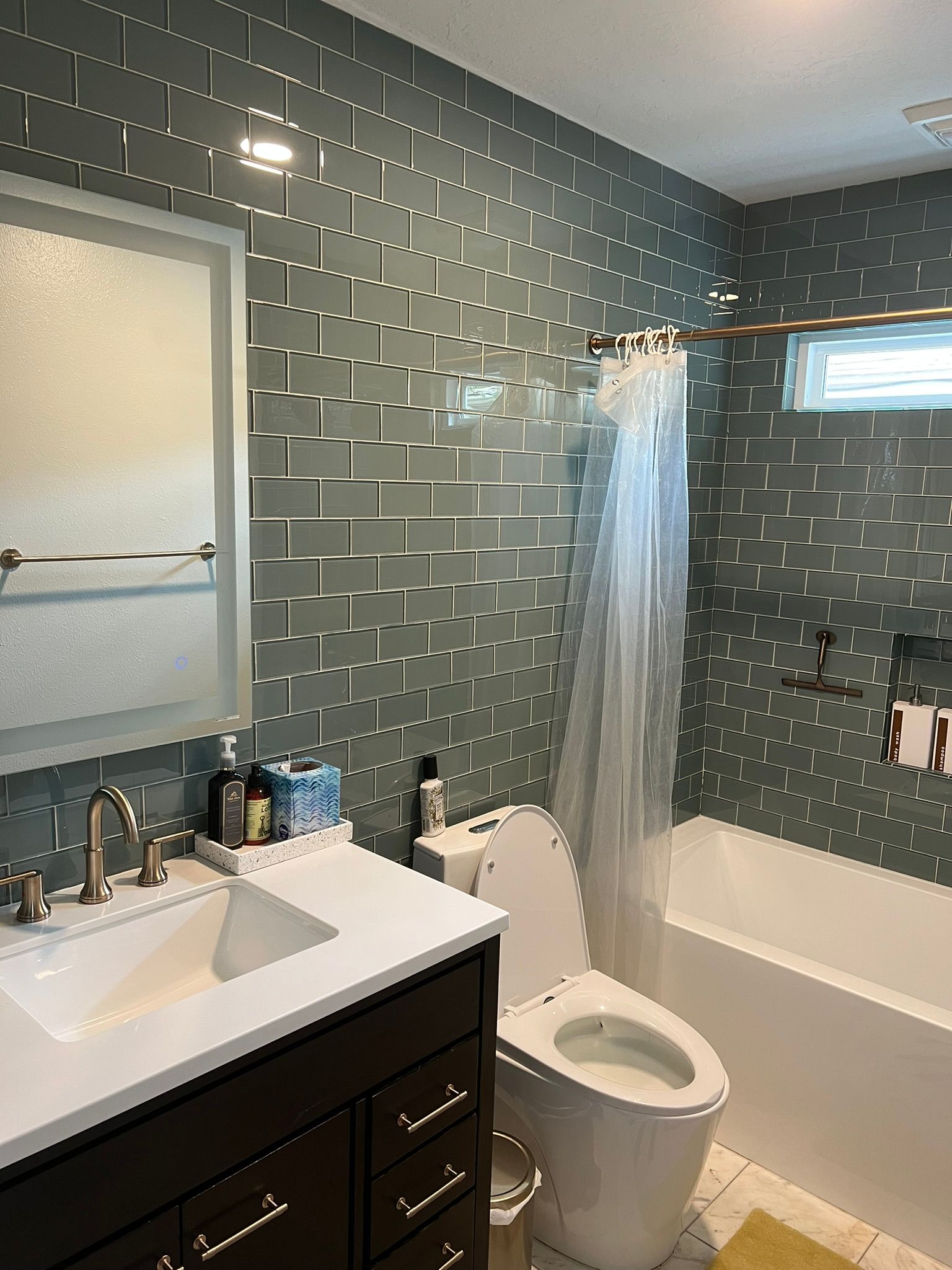 Small bathroom with gray tile walls, white vanity and toilet, and a bathtub with shower curtain.