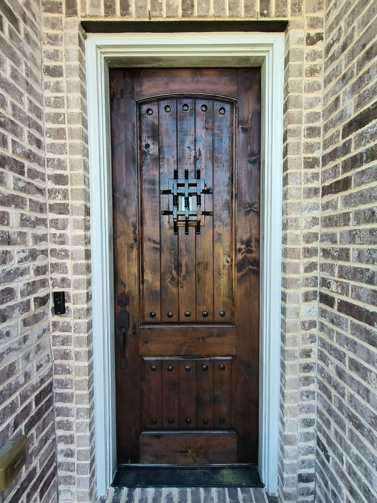 Dark wooden front door with wrought iron detail set in a brick doorway
