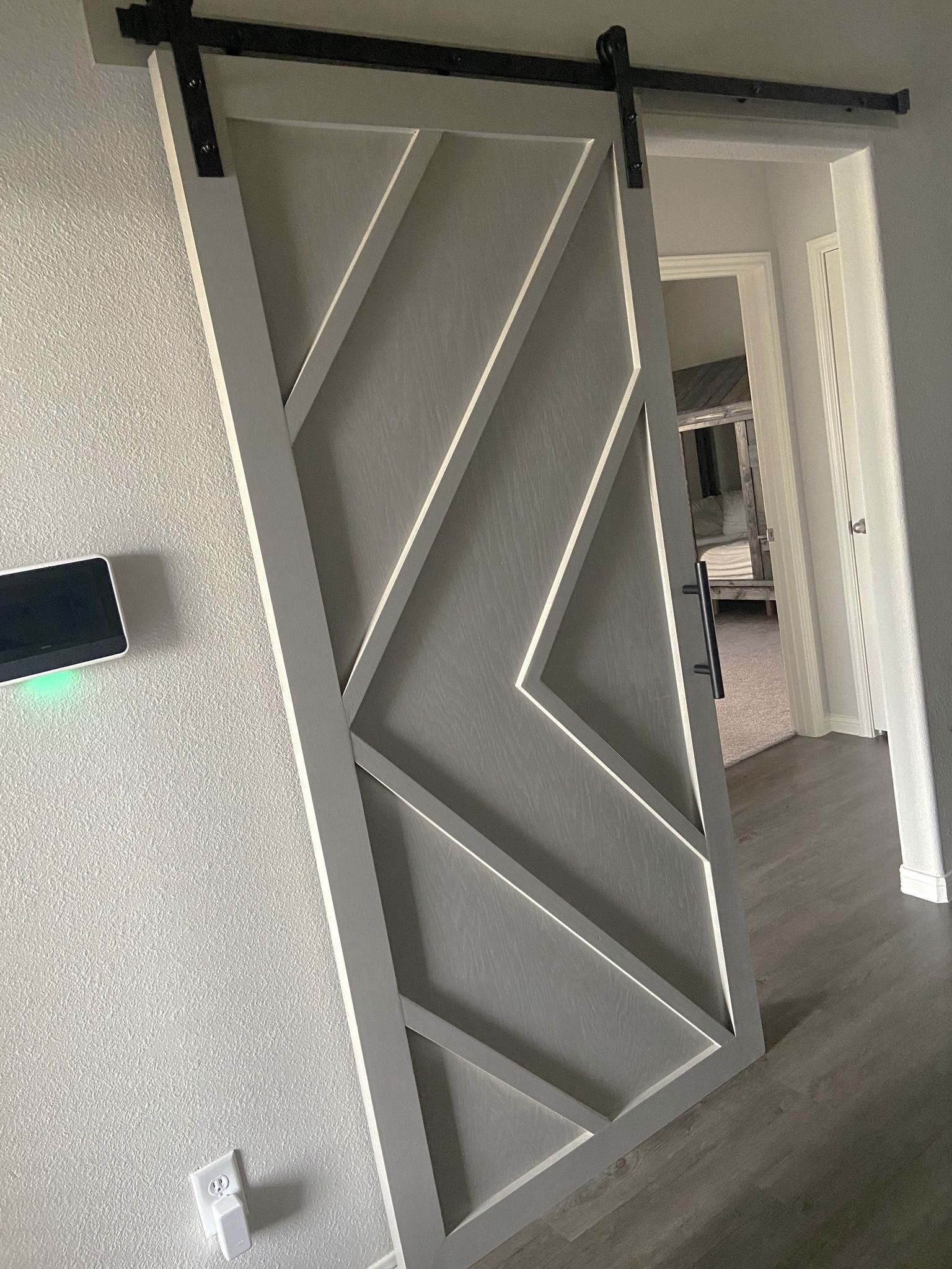 Gray geometric sliding door in a modern hallway with white walls and dark trim.