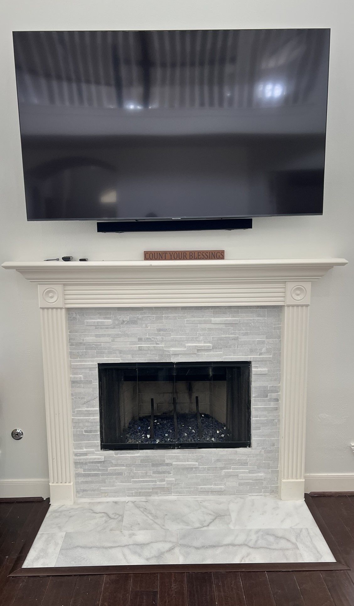 Living room fireplace with white mantel and tiled surround beneath a wall-mounted TV