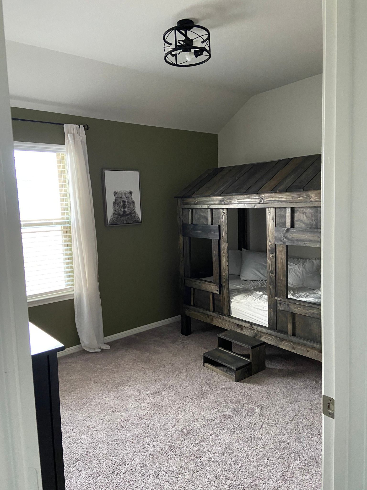 A carpeted bedroom with green walls, a loft bed, and a window with blinds.