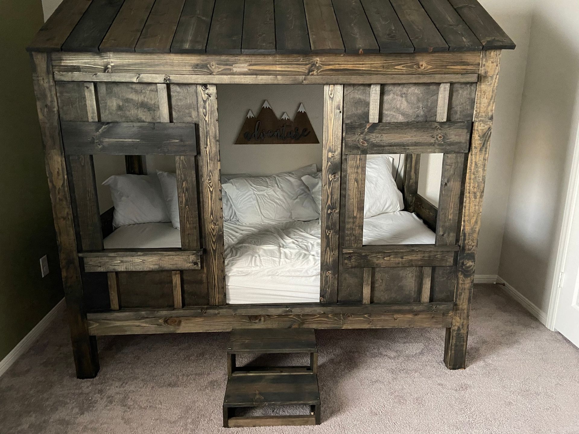 Rustic wooden pet bed with pillows, featuring three openings and a small step stool in a carpeted room