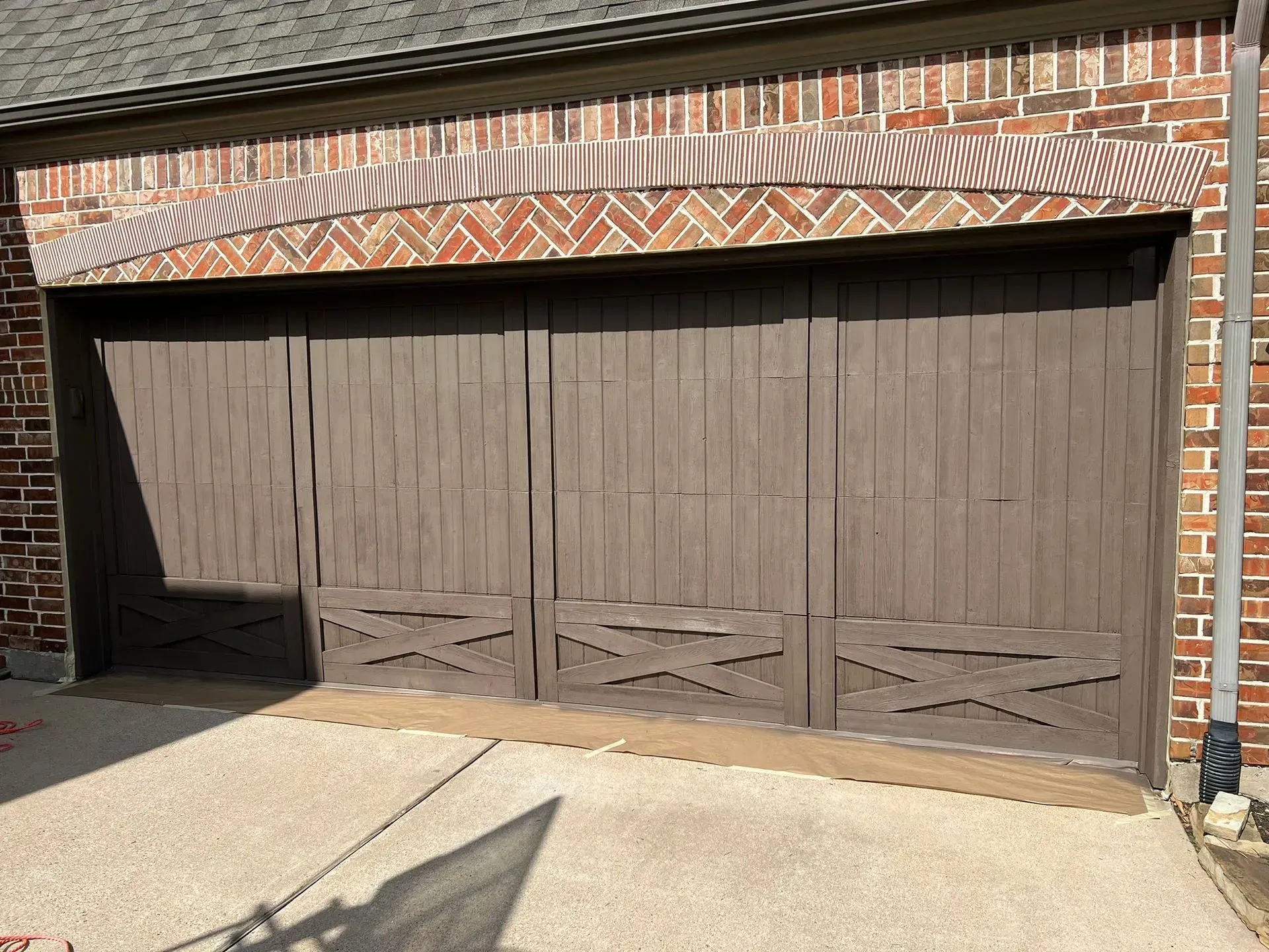 Brown double garage doors with a brick and decorative trim façade, seen in bright sunlight.