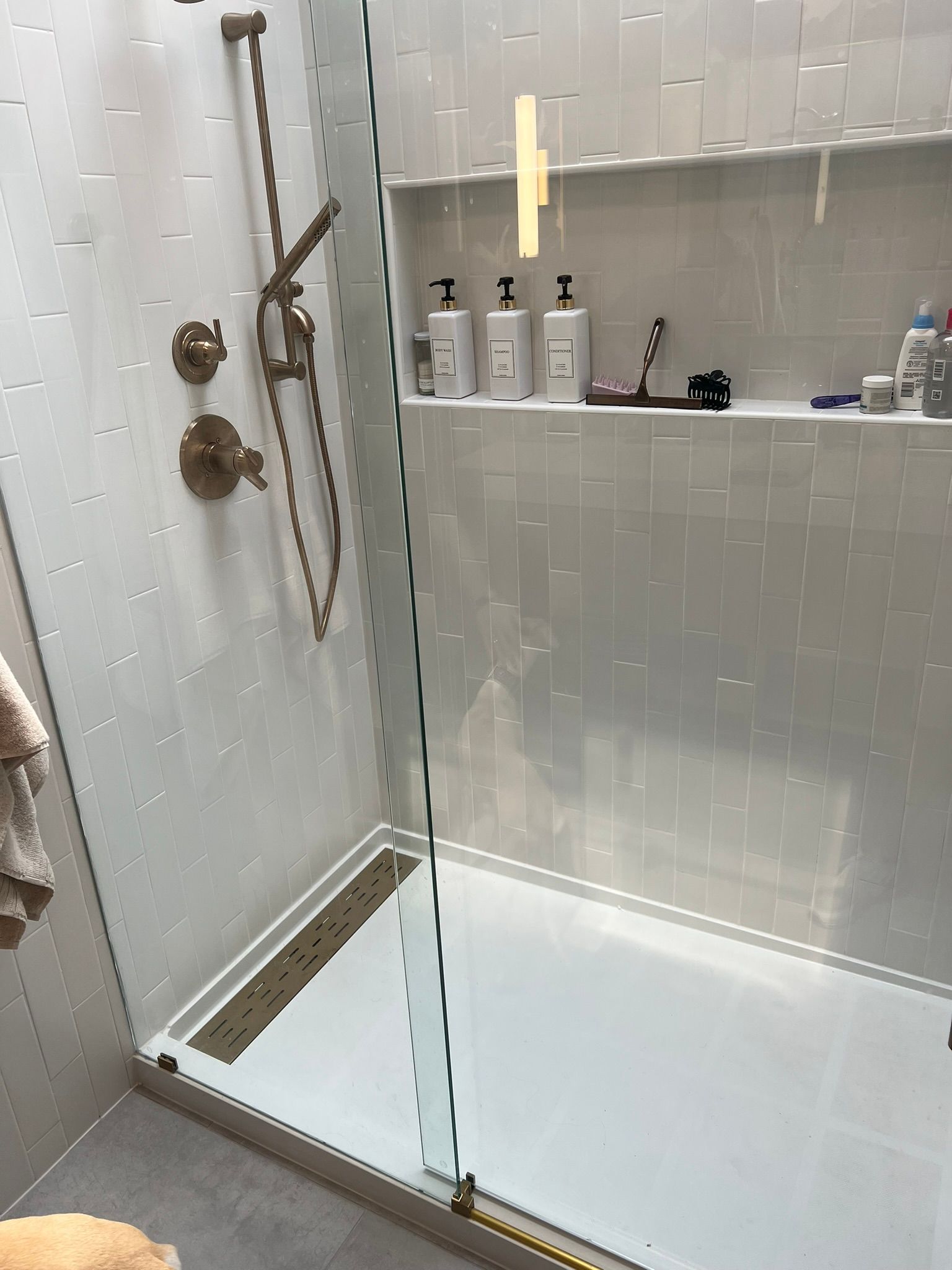 Modern tiled shower stall with glass partition, white floor, and wall shelves with toiletries