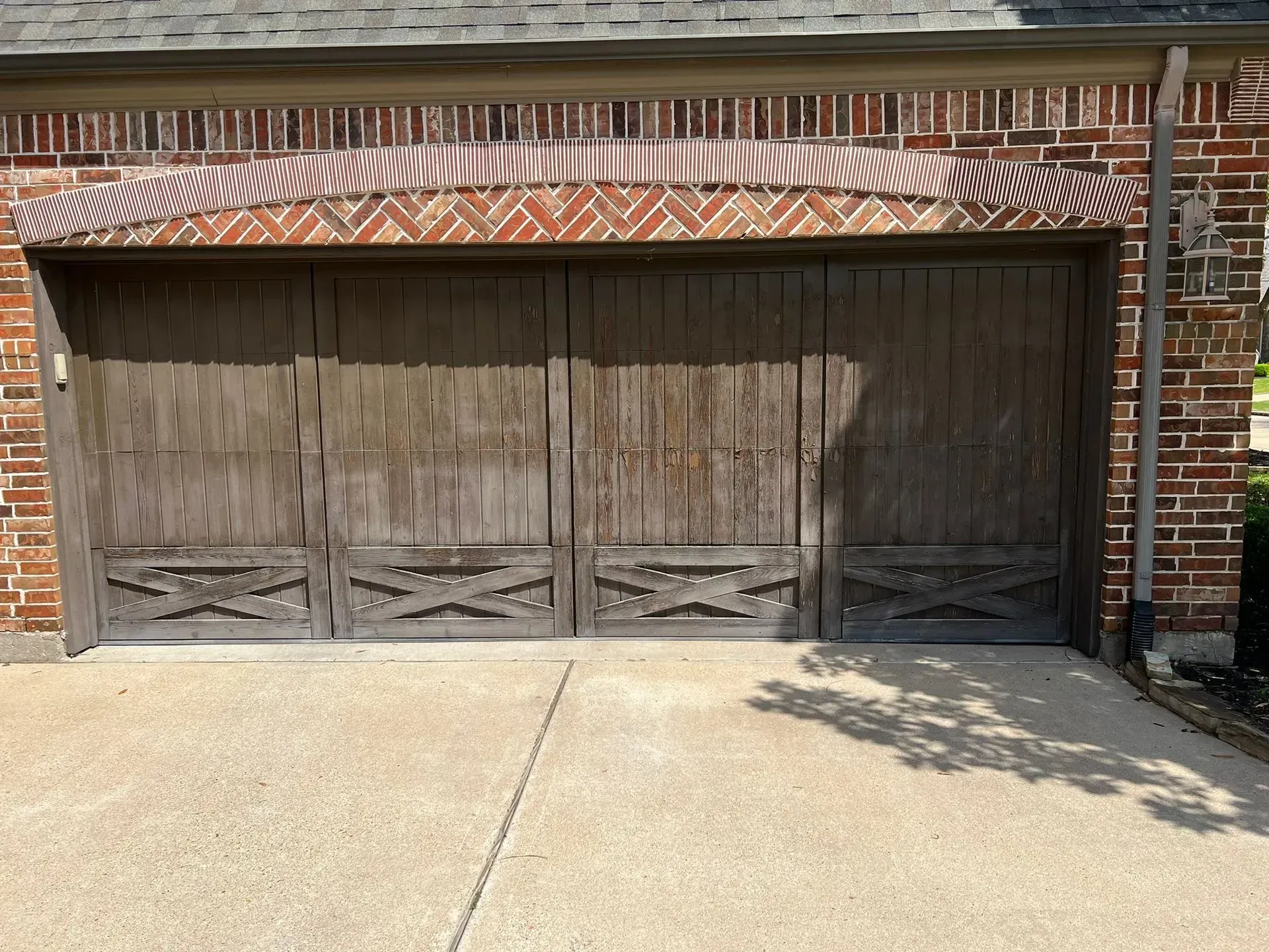 Wooden garage door on a brick house, with a concrete driveway in front.