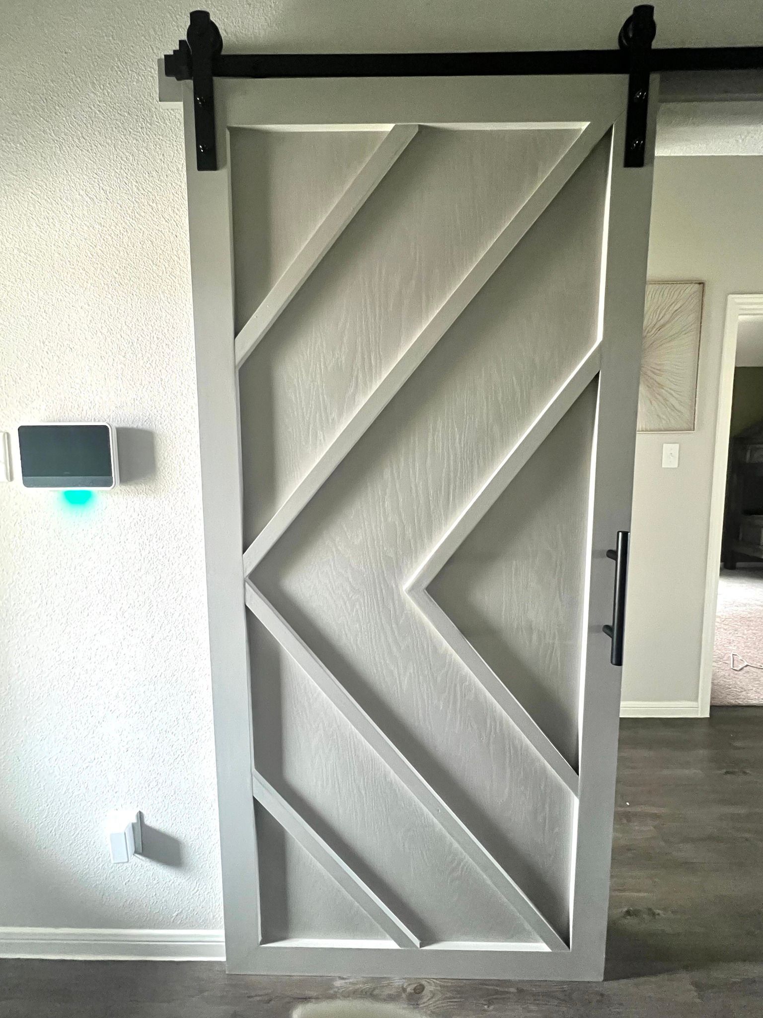 Gray barn-style sliding door with diagonal chevron slats in a white interior hallway