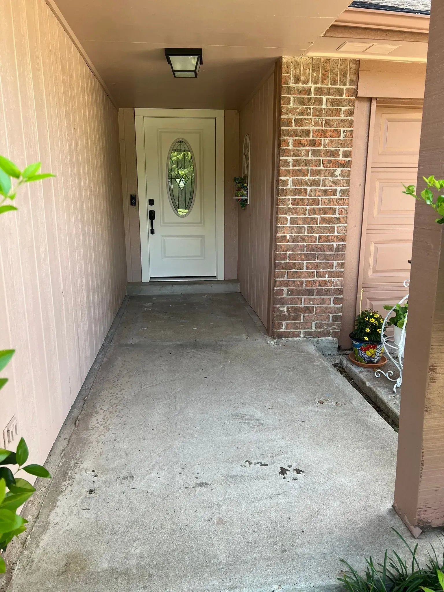 Covered front porch with concrete walkway, white front door, brick column, and potted flowers.