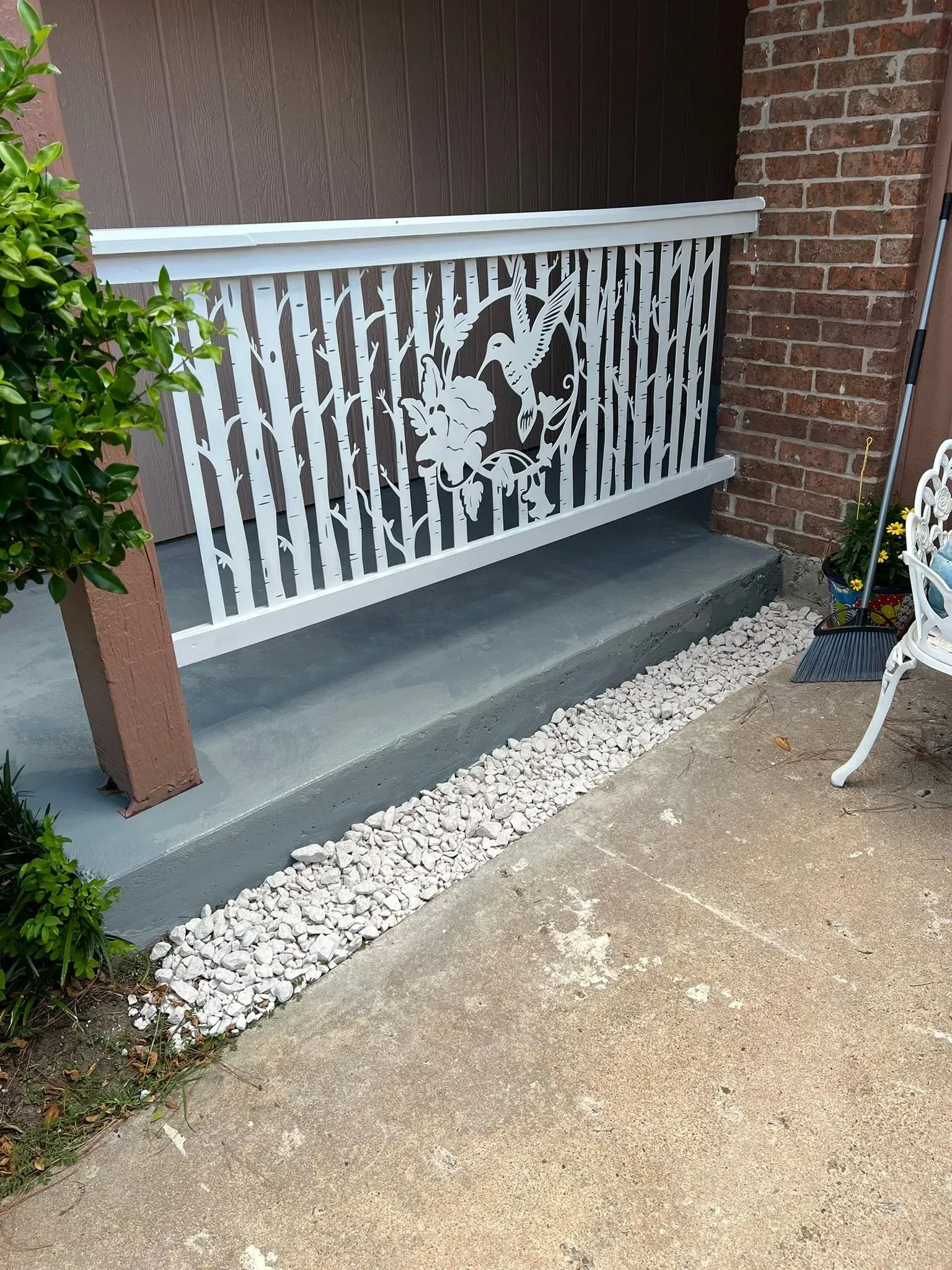 White railing beside a brick house, with a concrete step and gravel border along the walkway.