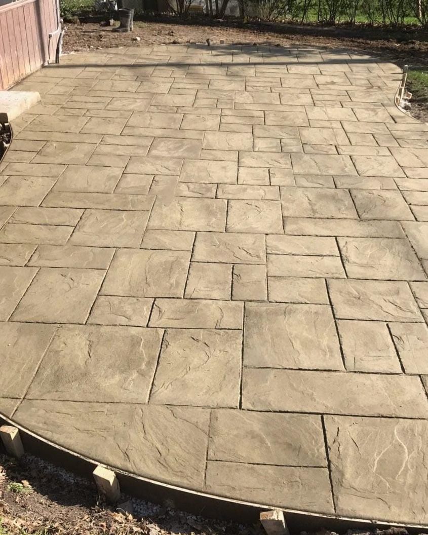 Stamped concrete patio with curved edge, leading to a yard and brick wall.