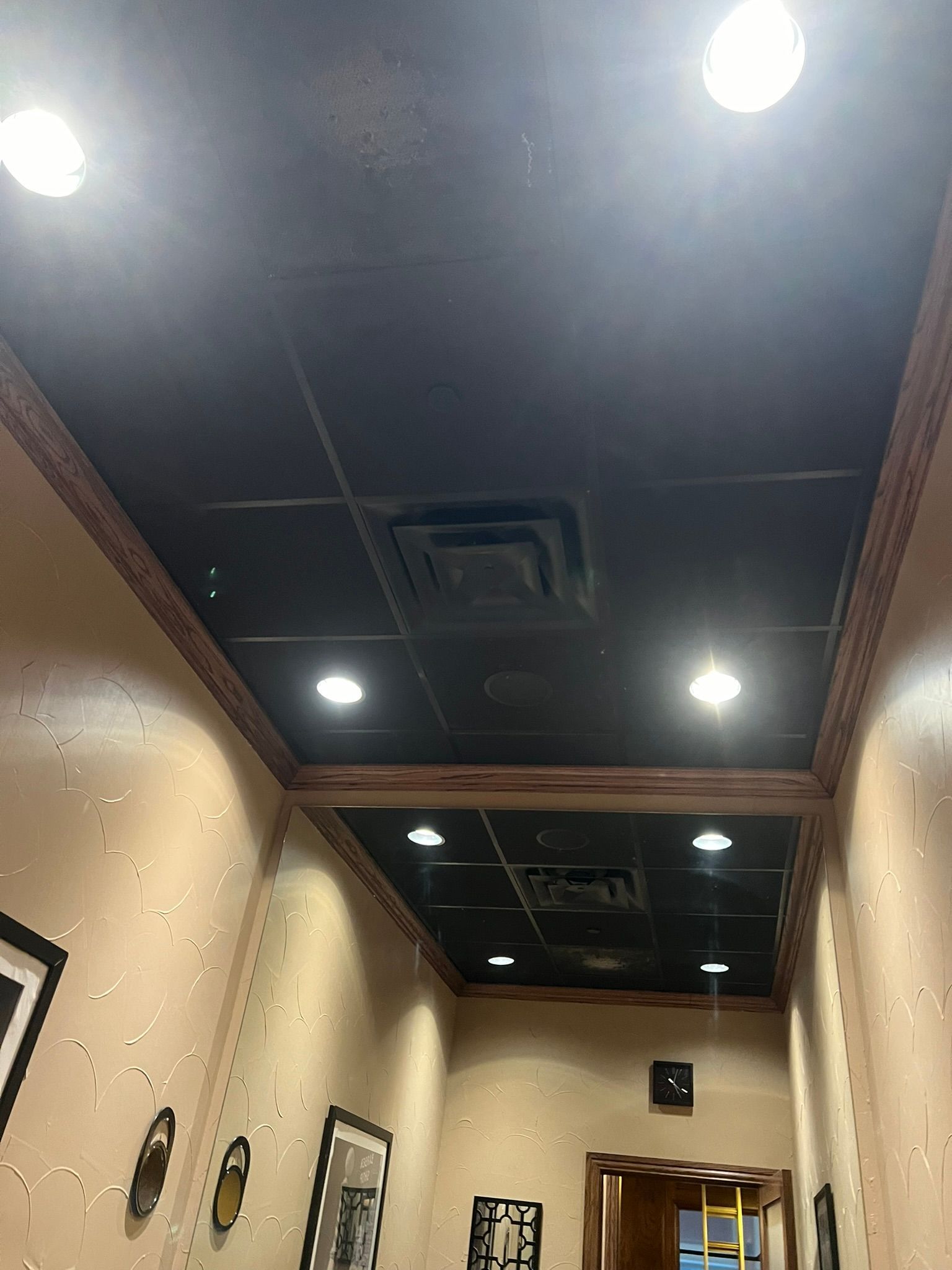 Narrow hallway with framed art, recessed ceiling lights, dark ceiling, and beige walls