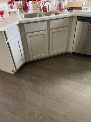 Kitchen sink and gray cabinets with white countertops and dark wood flooring.