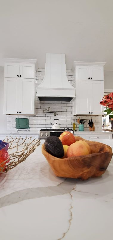 White kitchen with a fruit bowl on the counter and a stove centered under a hood.