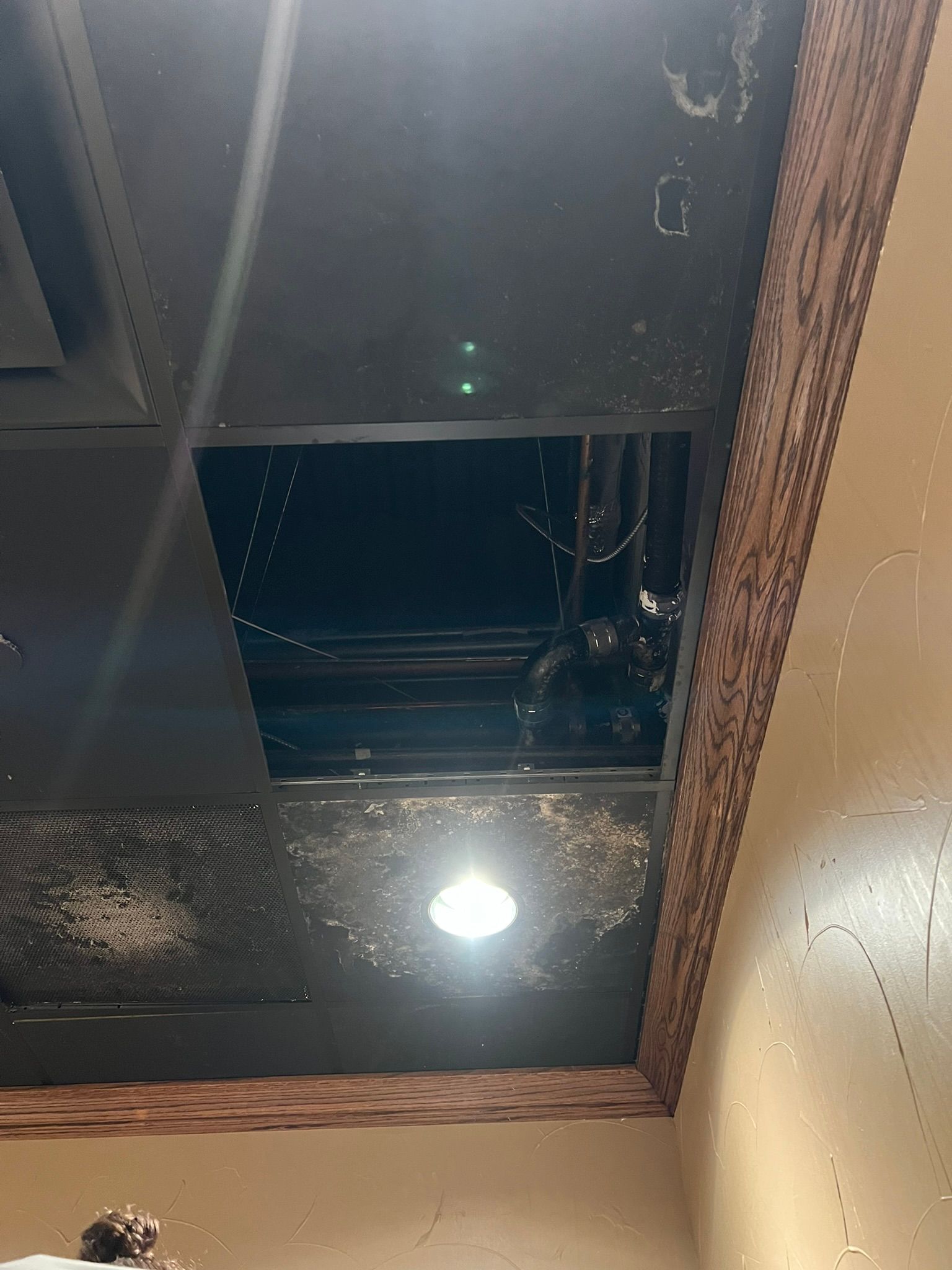 Ceiling with a dark open panel, bright recessed light, and beige walls, viewed from below