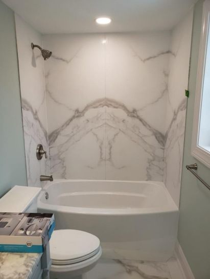 Modern bathroom with white marble-pattern shower wall, bathtub, toilet, and window light