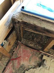 Damaged floor opening with exposed wood framing, debris, and a red-stained surface underneath