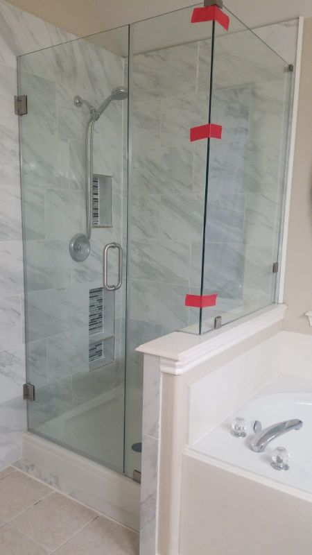Modern bathroom with glass shower enclosure, marble walls, and a white bathtub edge in the foreground