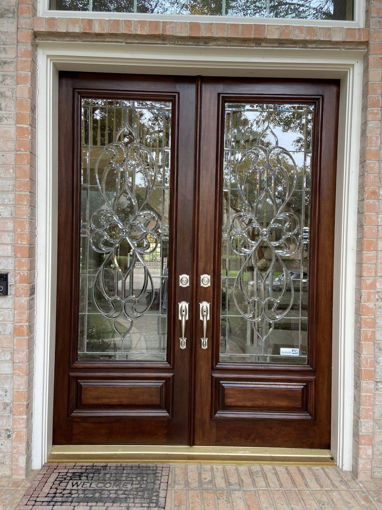 Wooden double front doors with glass panels and decorative metalwork in a brick entranceway