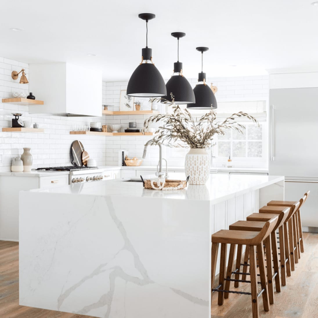 Bright white modern kitchen with marble island, black pendant lights, and wooden bar stools