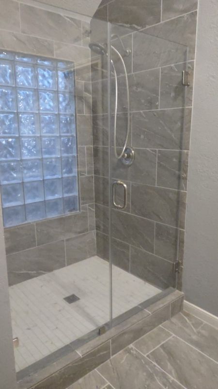 Modern tiled walk-in shower with glass enclosure, built-in bench, and frosted window light.