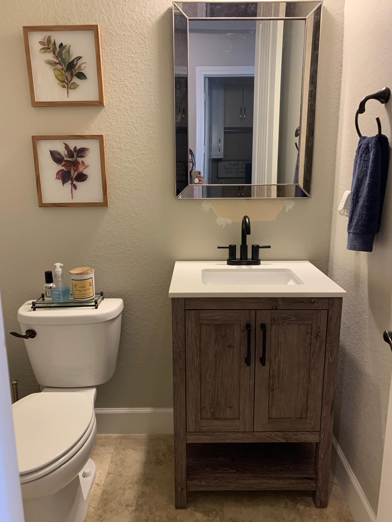 Small bathroom with toilet, vanity sink, mirror, wall art, and navy towel on the right.
