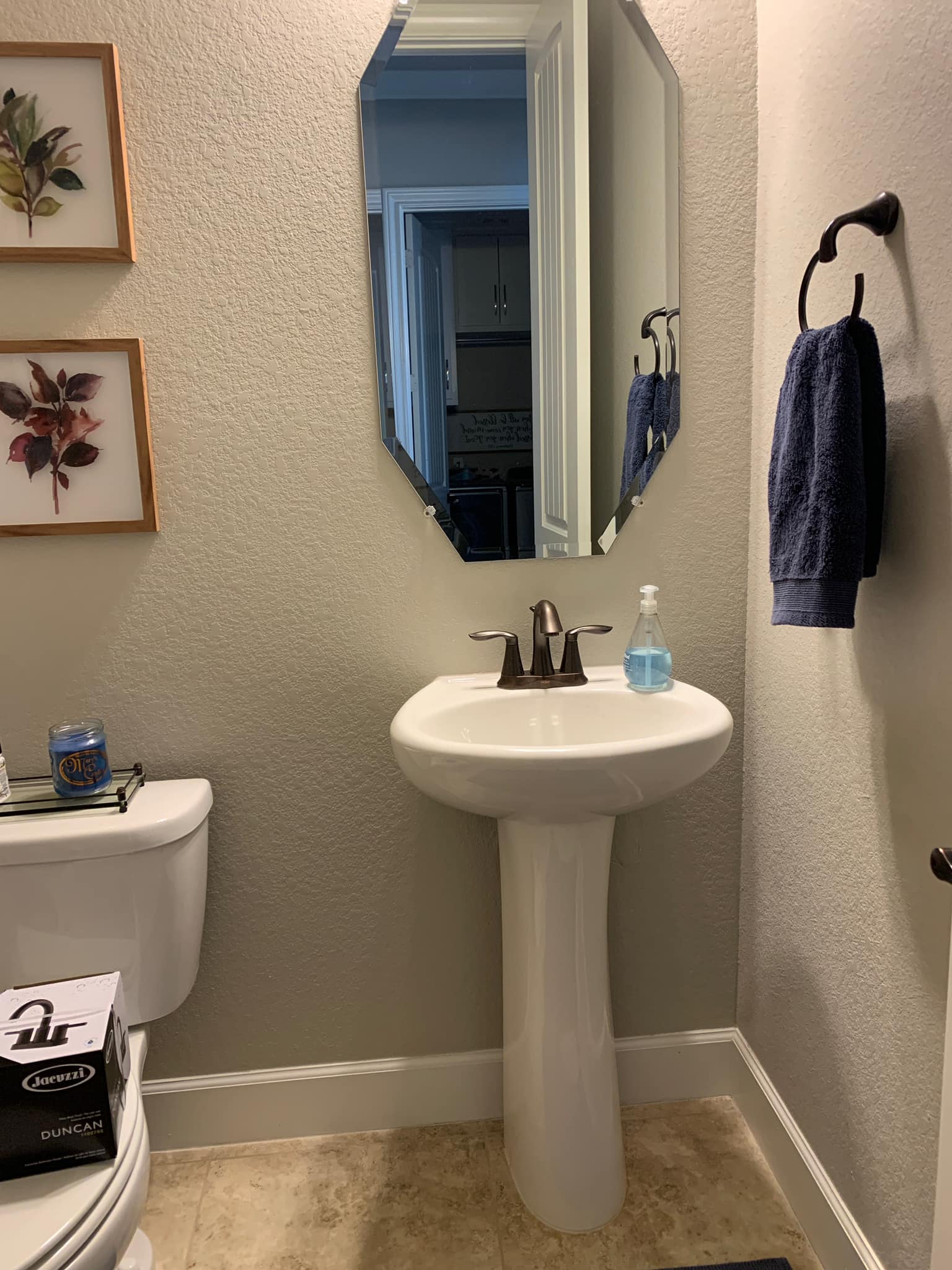 Small bathroom with pedestal sink, mirror, toilet, towel rack, and framed wall art.