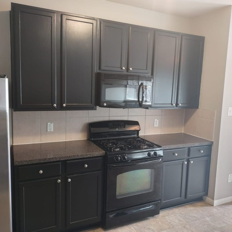 Small kitchen with dark cabinets, black stove and microwave, and beige tile backsplash