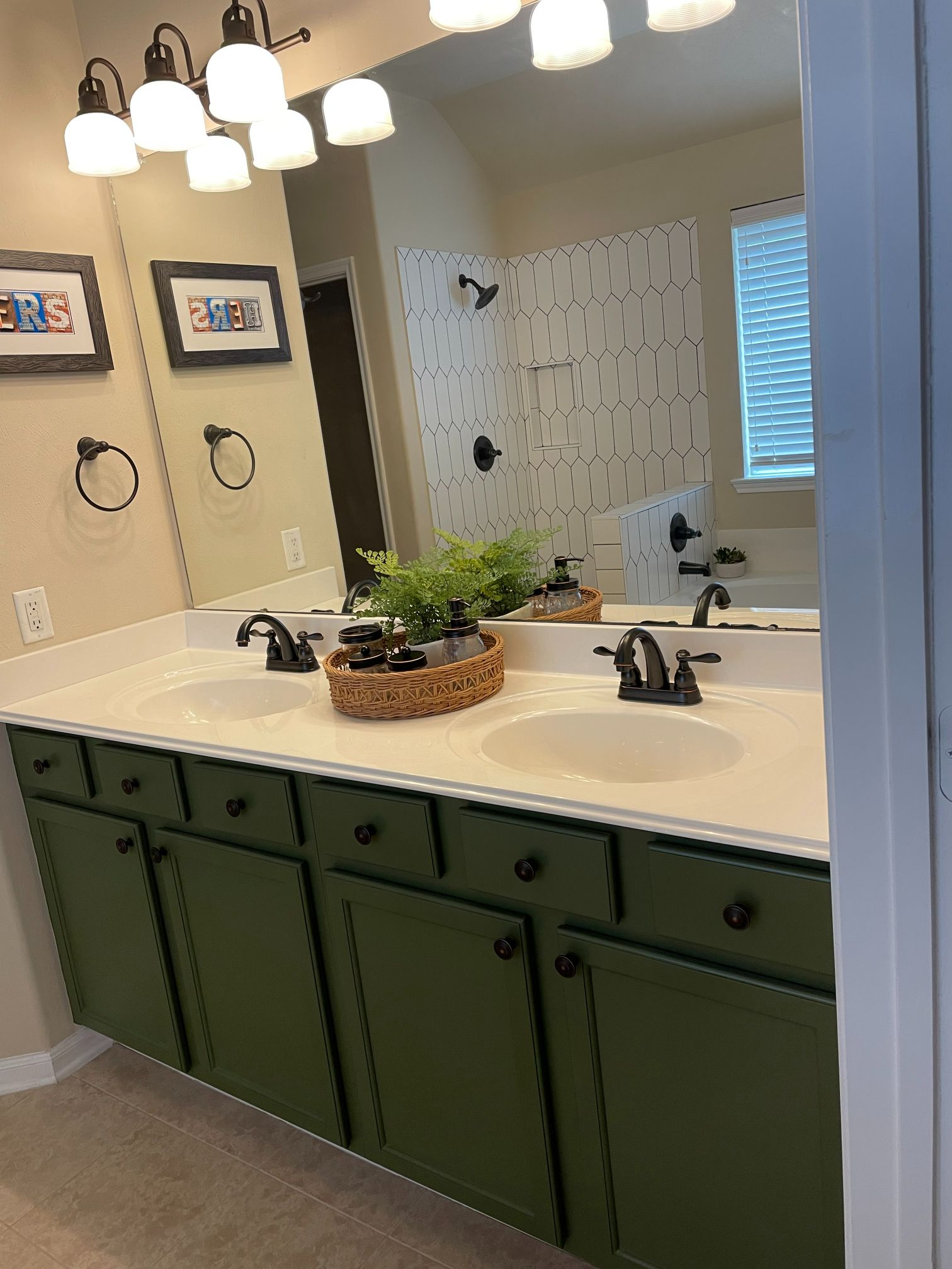 Bathroom vanity with green cabinets, white countertop, mirrors, and hanging lights