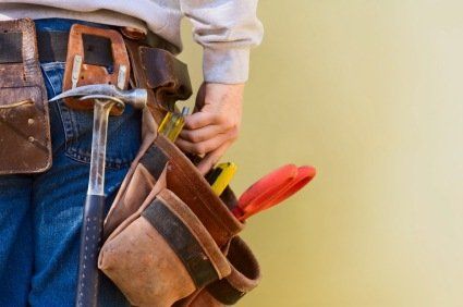 Tool belt with hammer, pliers, and red-handled tools on a worker’s waist against a yellow wall
