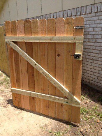 Wooden backyard gate with diagonal braces and latch beside a brick wall