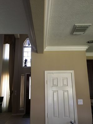 Interior hallway with beige walls, white door, and staircase leading to a tall arched window.
